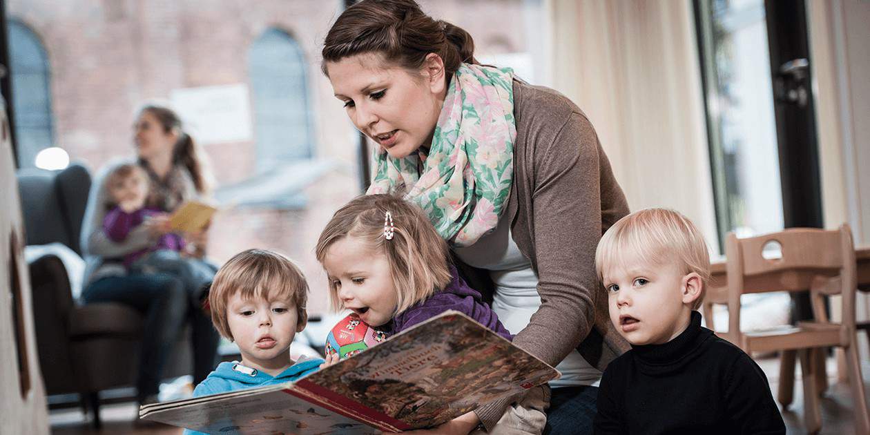 Eine Erzieherin der St. Marien Kita liest mit Kindern gemeinsam ein Buch.